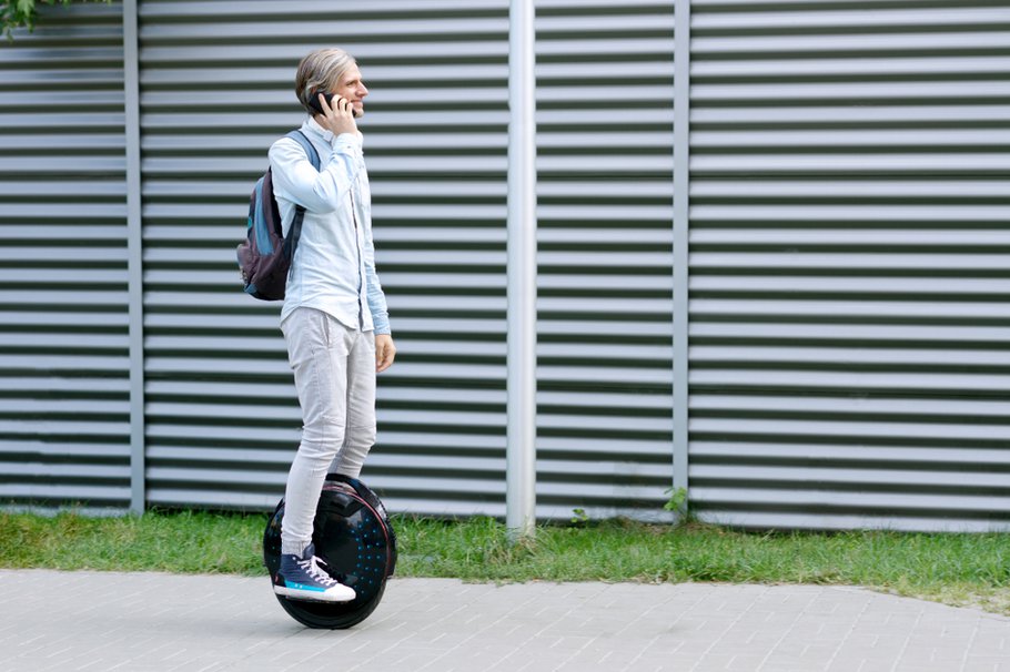 Modern young adult male businessman student freelancer riding driving on ecological electric transport futuristic eco electric unicycle scooter, balancing electric wheel with smartphone. Eco planet.