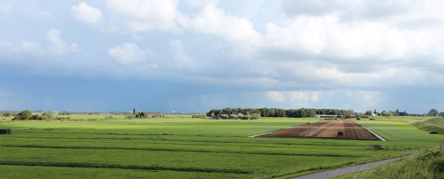 fields and meadows along dyke Hollandsche IJssel river with blue sky and whit clouds. The polder behind the dyke is named zuidplaspolder and the lowest area in the Netherlands with 21ft below sea