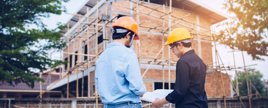 Two engineering man with helmet and paper work are discussing about the project over construction site background.