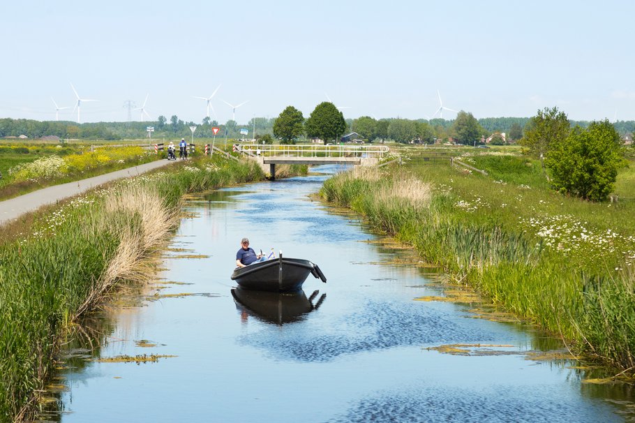 A small boat on the water and cyclists along the water in the nature reserve at Nijkerk.