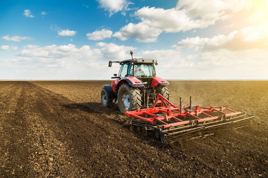 Landbouwer in tractor bereidt grond met zaaibedbebouwer als onderdeel van voorzaaiactiviteiten in het vroege voorjaar van landbouwwerken op landbouwgronden.