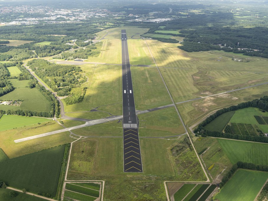 31 July 2017, Enschede, Holland. Aerial view of Twente Airport, a former military Dutch airforce base. The black runway is surrounded by green grass. A cloud shade is over the field.